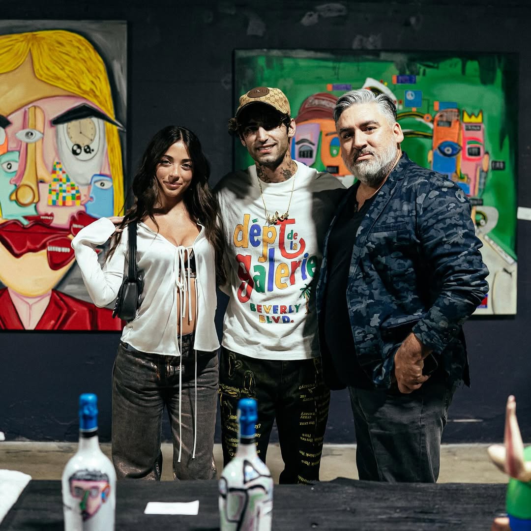 Three people posing in front of colorful artwork in an art gallery.