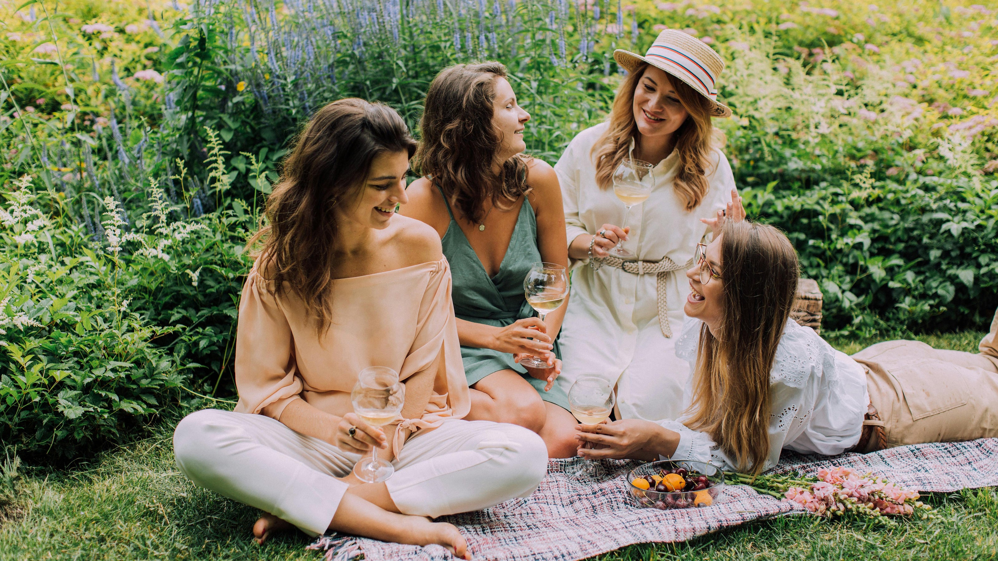 Four friends sharing wine on a picnic blanket in a garden