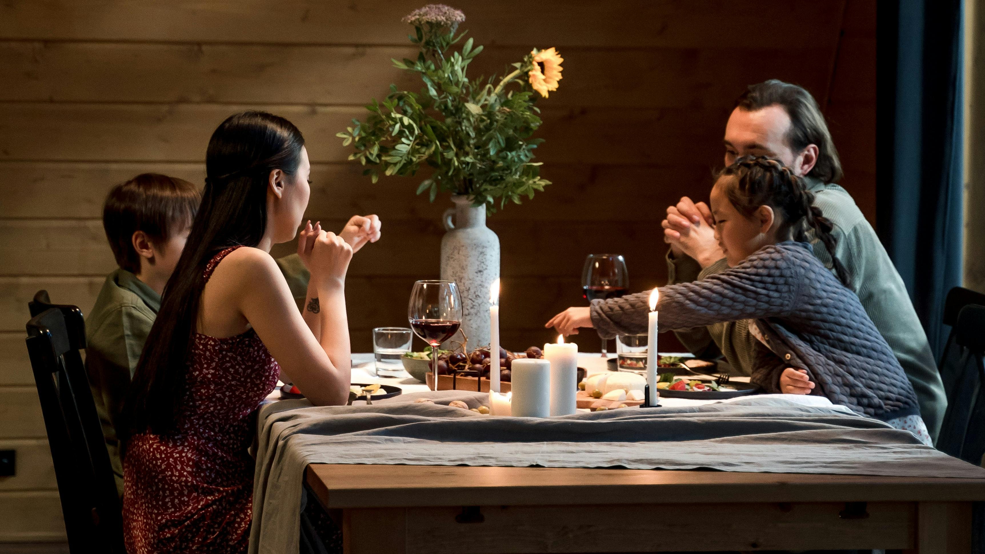 People sitting around a wooden dining table in a dimly lit room with a vase of flowers on the table.