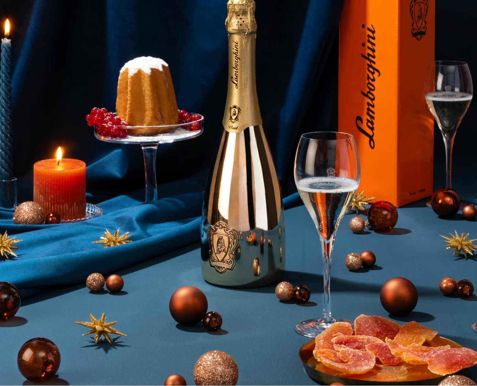 Lamborghini champagne bottle with glasses, a cake, and decorative items on a blue surface.