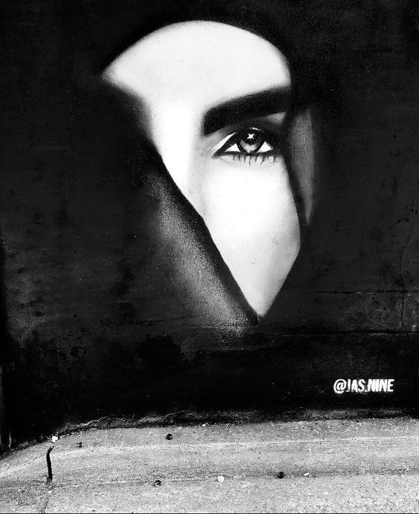Black and white mural of a face with a single eye on a wall.