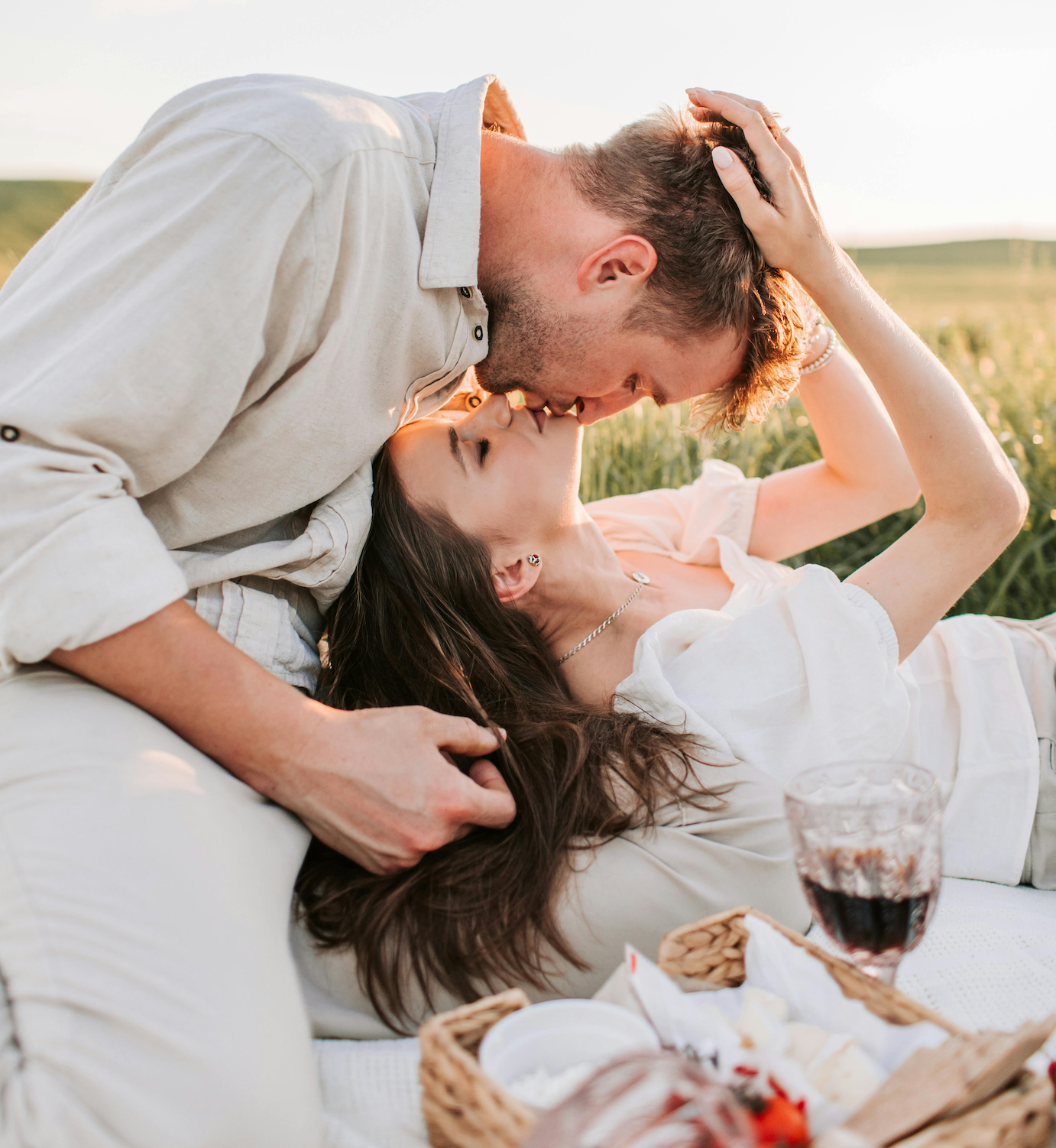 Couple sharing a romantic moment on a blanket in a field with a picnic basket.