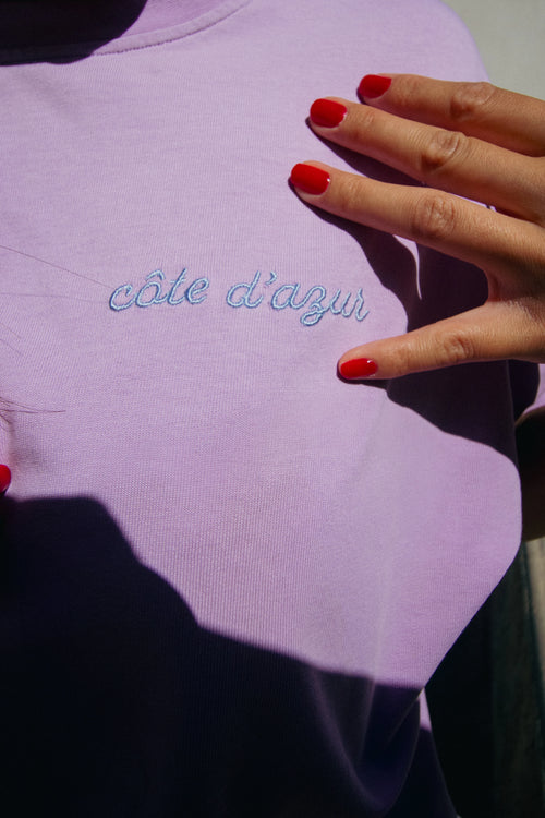 Pink sweatshirt with 'côte d'azur' embroidery and a hand with red nails holding it.