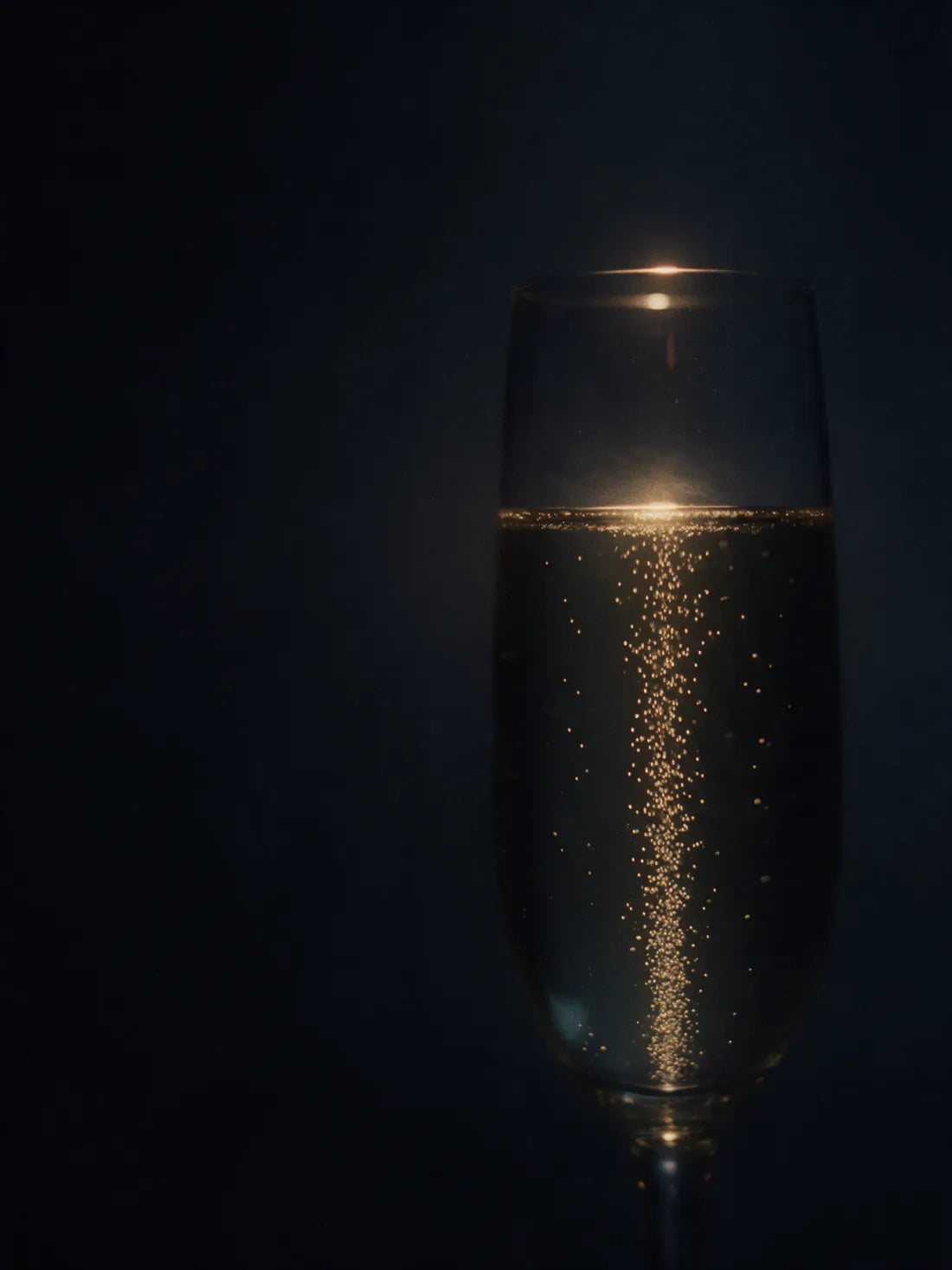 A fine column of bubbles rising through pale gold sparkling wine in a glass